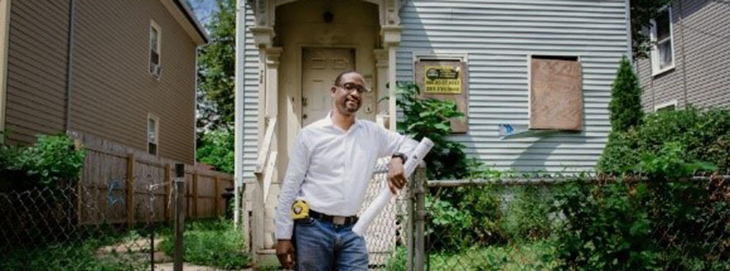 Man standing in front of an older urban home in need of repair
